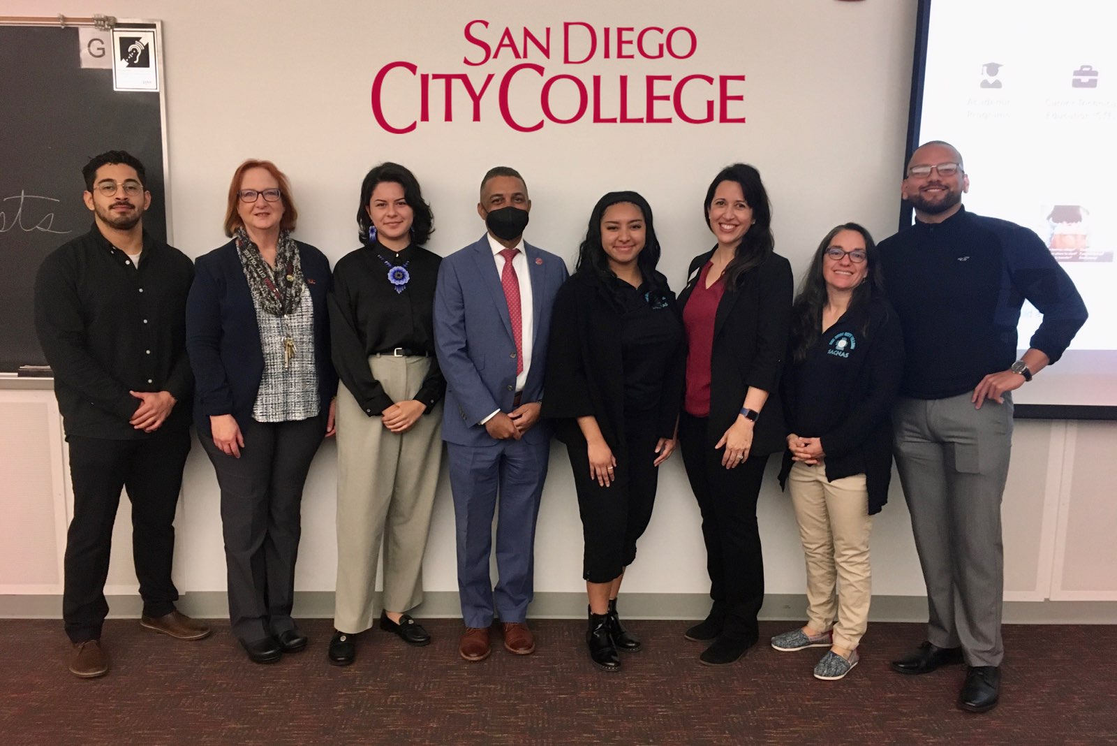 At San Diego City College 3 scholars present at San Diego City College. There are a group of 8 people in the picture. They are all in dress clothes. The President of City College is waring a mask and The Dean of Sciences at City is also present.