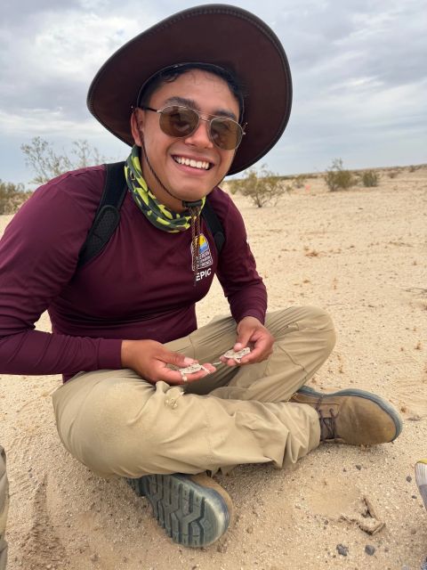 Summer 2026: Cesar Edeza sits in the desert holding a flat tailed lizard. They have a hat on , sunglases and protective sun attire. This summer he did an internship working as a Flat- Tailed Lizard Technician at El Centro Field Office by the American Conservation Expereince.